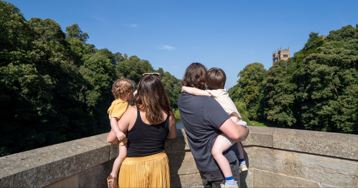 Family of mam, dad and two children stood on bridge admiring view in Durham City on a bright sunny day.